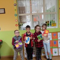 Czwórka dzieci stojąca obok siebie i pokazująca wykonane kartki, widać liście w kolorach: niebieskim, żółtym i zielonym przyklejone do kolorowych kartek papieru