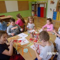 Dzieci podczas wykonywania prac plastycznych wybierają paski z kolorowego papieru i przyklejają je do ilustracji drzewa.