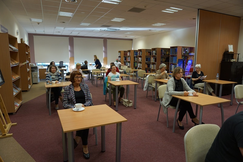 Zebrani goście siedzą przy stolikach i słuchają prelekcji.