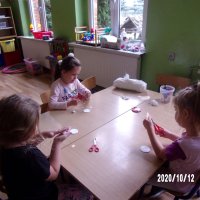 Trzy dziewczynki pracujące na zajęciach, dwie wycinają elementy z papieru, trzecia dziewczynka robi kulki w waty.