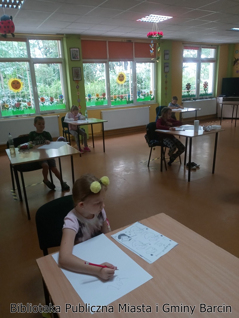 Dziewczynka korzystając z instrukcji rozpoczyna rysowanie swojej pracy, w dalszym planie pozostałe dzieci również postępują tak samo.