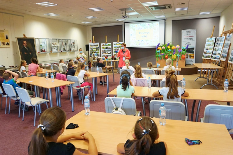Panie bibliotekarki z oddziału dla dzieci rozpoczynają spotkanie, zebrane dzieci siedzą przy stołach.
