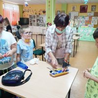 Pracownica świetlicy pomaga dzieciom przymocować maszt wykonany z wykałaczki i trójkątnego kawałka papieru do łódki wykonanej z wytłaczanki do jajek.