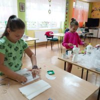 Dwie dziewczynki pracujące prz swoich stanowiskach wykonując pracę złożoną z różnych materiałów.