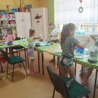 Kolejny etap prac, w którym dzieci wsypują piasek i kolorowe kamyki.