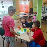 Trzej chłopcy rozwiązują zadanie z kolorowymi kubeczkami.