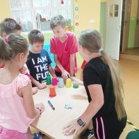 Dzieci korzystając z pięciu kubków w różnych kolorach rozwiązują zadanie przygotowane przez prowadzącą.