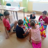 Piątka dzieci siedzi na podłodze i układa dwie kubeczkowe piramidy.