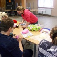 Uczestniczki spotkania siedzą przy stołach i szydełkują.