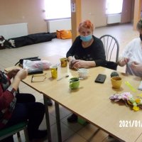 Uczestniczki spotkania siedzą przy stołach i szydełkują.