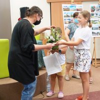 Dwie dziewczynki wręczające kwiaty i upominek drugiej prowadzącej.