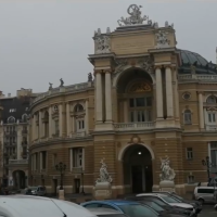 Na zdjęciu widać budynek o elewacji w kolorach żółto beżowych z licznymi kolumnami i rzeźbami na dachu, główny budynek jest półokrągły, przed wejściem ustawione są ozdobne figury.