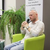 Pan Wojciech siedzi na fotelu i słucha wypowiedzi jednego z uczestników spotkania.