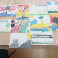 Prace uczestników zajęć, widać kolorowe krajobrazy, przeważają ilustracje zawierające słońce, kwiaty, drzewa i chmury.