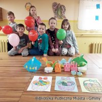 Grupowe zdjęcie dzieci uczestniczących w zajęciach, dzieci trzymają balony a przed nimi leżą wykonane koszyczki i pokolorowane obrazki.