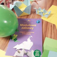 Zdjęcie książki zatytułowanej "Modułowe zabawy czyli origami modułowe z kwadratu", książka leży na stole pomiędzy wykonanymi koszyczkami.