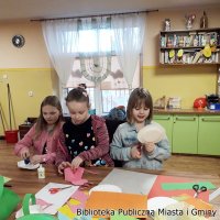 Zdjęcie trzech dziewczynek, pierwsza zszywa zszywaczem papierowy talerzyk, druga skleja koszyczek z  różowego papieru, trzecia nacina papierowy talerzyk.