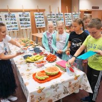 Dzieci ustawione w kolejce biorą przybory kuchenne takie jak deski do krojenia i nożyki.