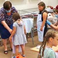 Dyrektor razem z pracowniczką biblioteki zakłada dzieciom fartuszki.