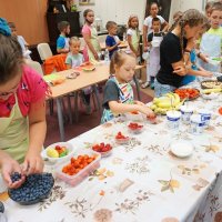 Dzieci biorą składniki do przyrządzenia zdrowych przekąsek, tymi składnikami są: arbuzy, truskawki, borówki, banany i daktyle.