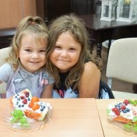 Dwie dziewczynki z wykonanymi na zajęciach przekąskami uśmiechają się wesoło.