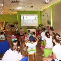 Dzieci siedzą na krzesełkach i oglądają nagranie pokazujące podwórkowe zabawy.