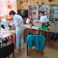 Grupa podczas pracy, dzieci stoją za stołami na których leżą kartony, kolorowy papier i klej.