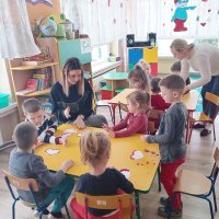 Na zdjęciu widać dwie grupy pracujących dzieci, przy każdej z grup jest opiekunka, która pomaga dzieciom w zadaniu.