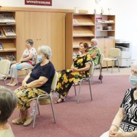 Na zdjęciu po lewej stronie widać baner promujący autorkę, na środku jest ekran rzutnika, na którym wyświetlany jest tytuł spotkania, po prawej na fotelu sieci pani Edyta Świętek i mówi do mikrofonu.