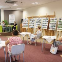 Na zdjęciu widać trzy uczestniczki spotkania, prowadzącą oraz zaproszonego gościa a pod ścianą stoją plansze z wystawianymi fotografiami.