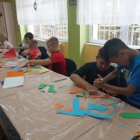 Dzieci pracujące na zajęciach wycinają kształty z papieru i sklejają je razem za pomocą kleju.