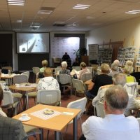 Zdjęcie z tyłu sali widać zaproszonego gościa na scenie i zebraną publiczność.