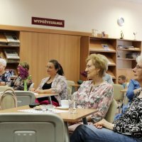 Zdjęcie części publiczności, widać ziedem osób siedzących przy stolikach i słuchających koncertu.