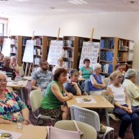 Zdjęcie części publiczności widać 18 osób siedzących przy stolikach i słuchających z uwagą zaproszonego gościa.