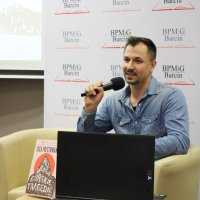 Maciej Piera z mikrofonem w ręce siedzi na fotelu i odpowiada na  pytania publiczności.