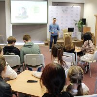 Zdjęcie z głębi sali widać 10 osób siedzących przy stolikach, oraz prowadzącego stojącego przed nimi.