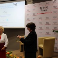 Pani Helena Wyrzykowska i dyrektor biblioteki Renata Grabowska stoją przed publicznością i rozmawiają.