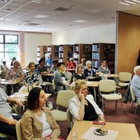Zdjęcie widowni, na którym widać osoby siedzące przy stolikach z ciastkami i kawą, słuchających opowieści Pana Michała Szulima