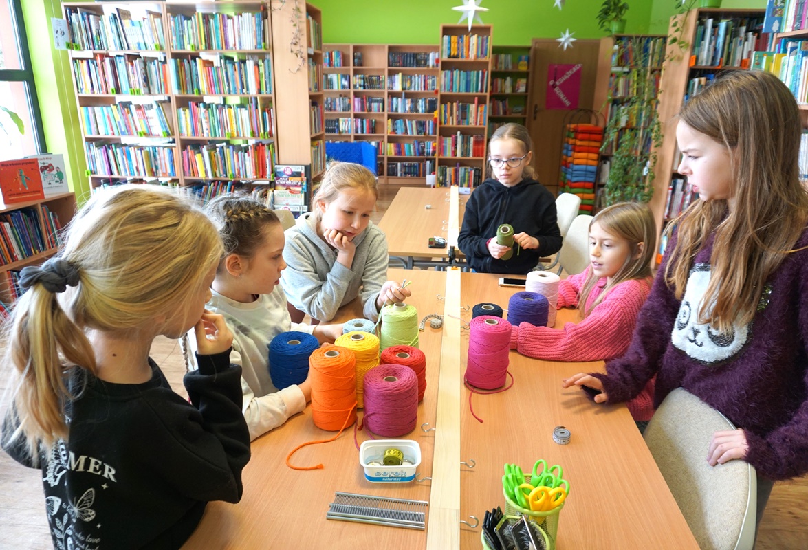 5 dziewczynek pracujących w trakcie zajęć, pomiędzy nimi na stole stoją motki z kolorowymi sznurkami.