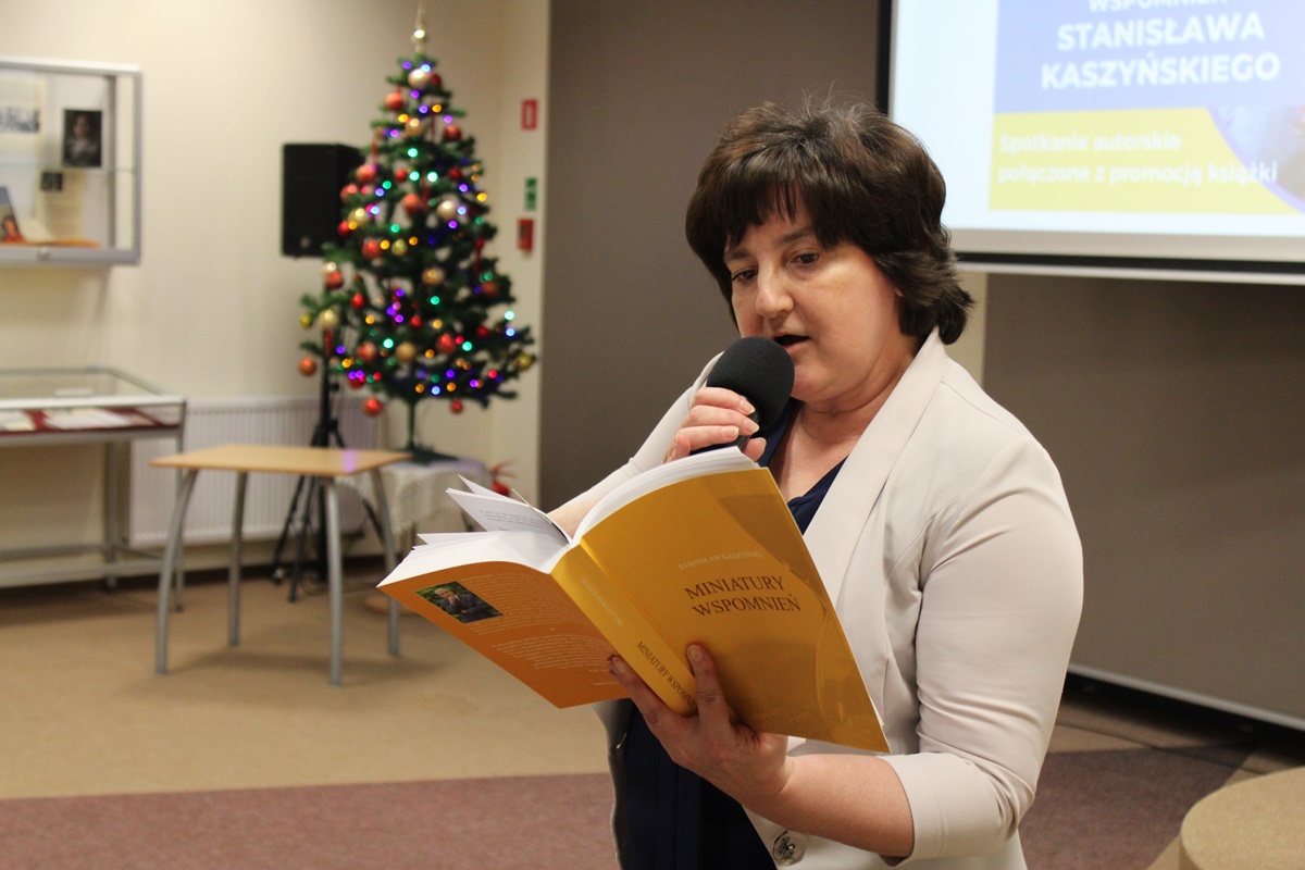 Dyrektor biblioteki trzyma w ręku książkę pt. "Miniatury wspomnień", czyta jej fragment do mikrofonu.