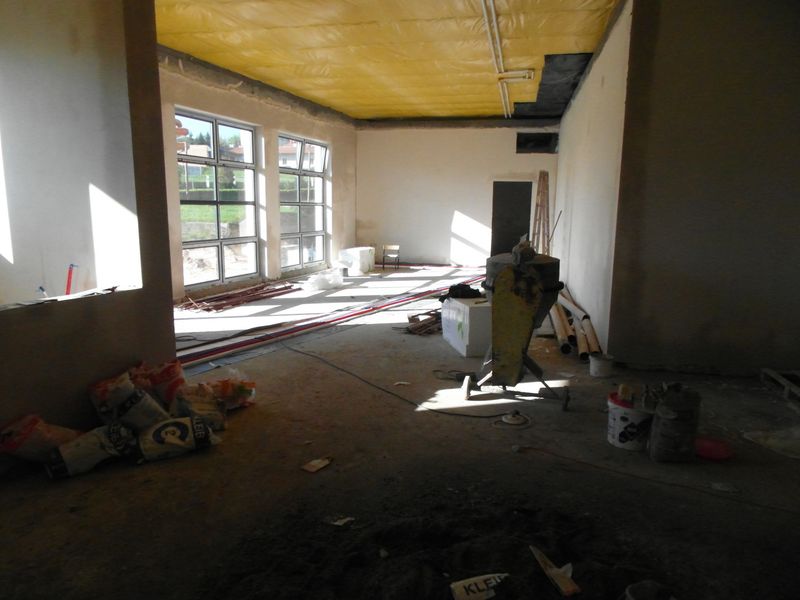 pomieszczenie obecnego oddziału dla dzieci i młodzieży podczas budowy, otynkowane ściany, betonowe posadzki, sufit poktyty żółtą folią, z przodu widać betoniarkę i puste worki po zaprawach budowlanych