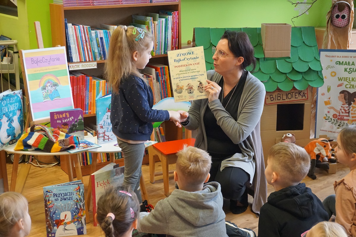 pracownica biblioteki prowadząca zajęcia wręcza dyplom za udział dziewczynce reprezentującej klasę która brała udział w zajęciach