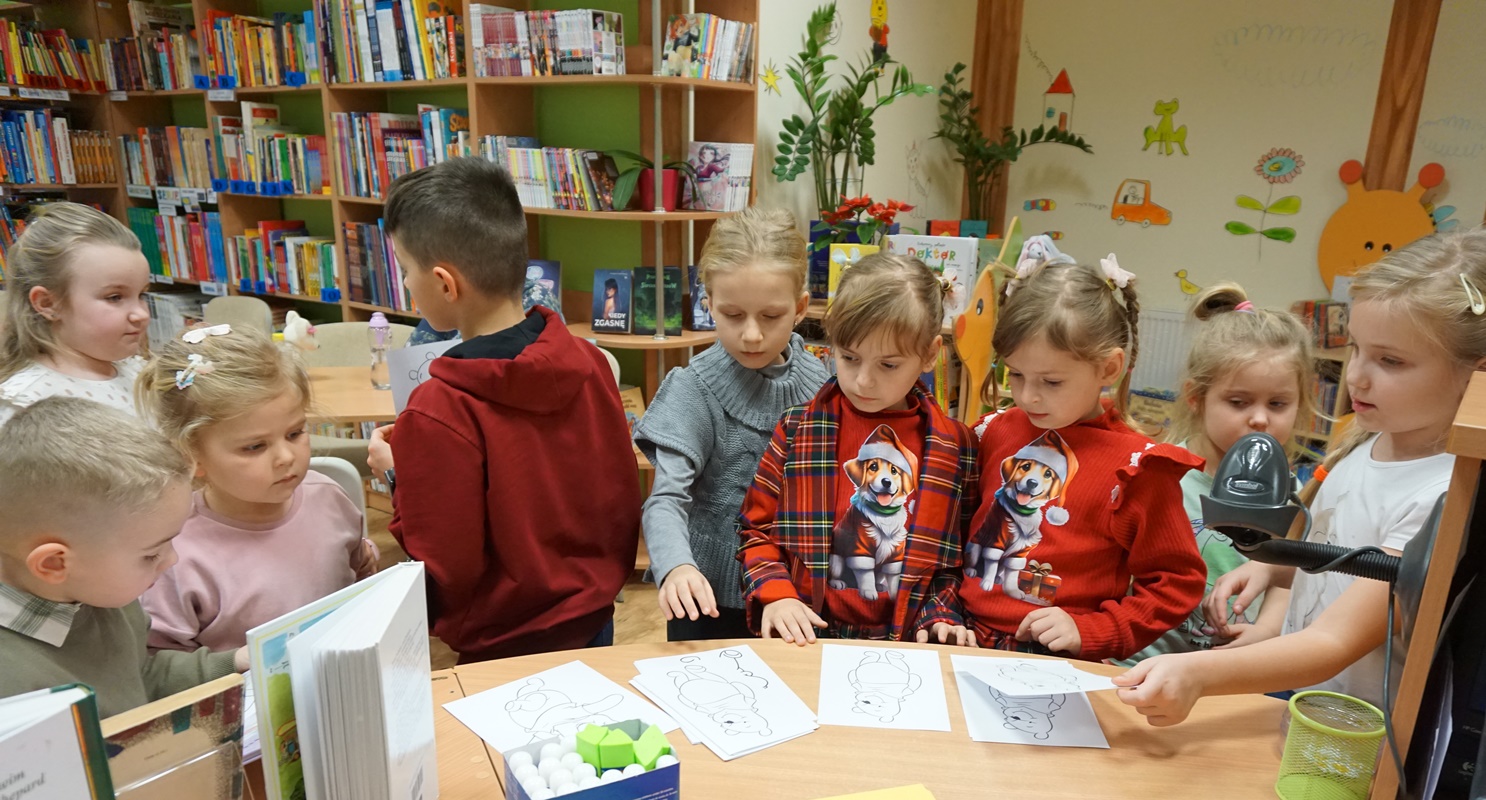 dziewięcioro dzieci stoi koło lady bibliotecznej na której leżą przygotowane do pracy wizerunki kubusia puchatka