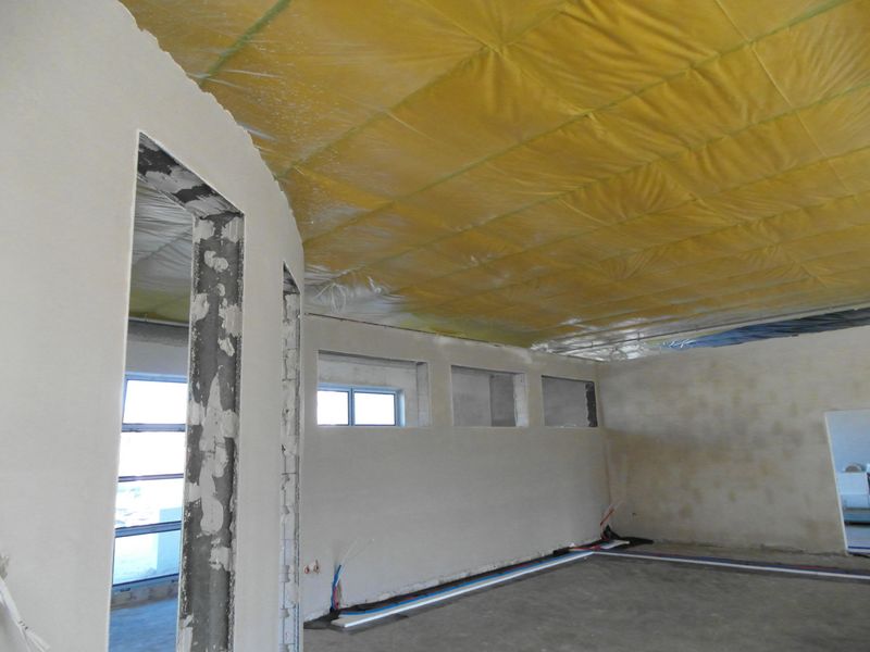Wnętrze budynku otynkowane ściany, żółta folia pod sufitem, betonowe posadzki