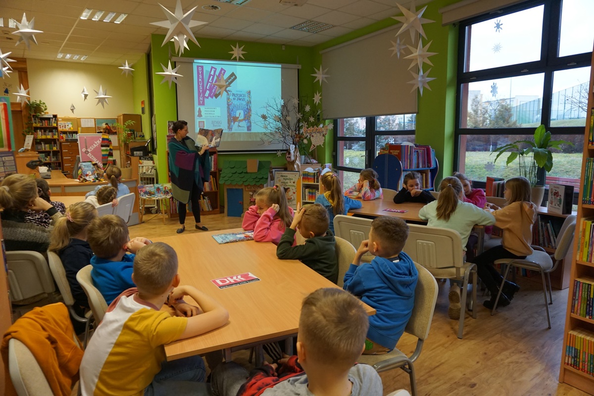 Bibliotekarka prowadząca zajęcia czyta i pokazuje dzieciom książkę omawianą na zajęciach