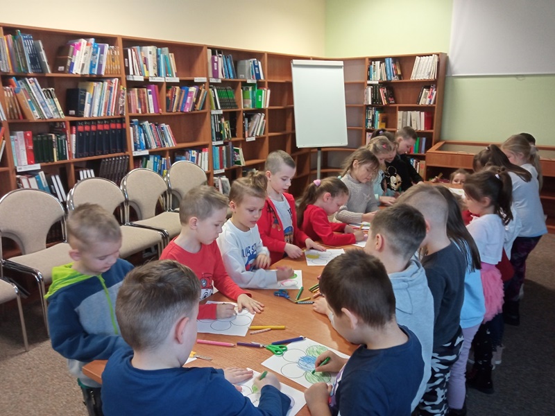 Dzieci przy stołach kolorują obrazki przypominające główkę kwiatu ( pięć kół wokół jednego koła w środku)