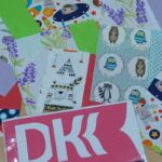 Leżące na stole różnokolorowe kartki z podobiznami zwierząt takimi jak niedźwiedzie, sowy, ptaki, jedna z kartek prezentuje różowo czarne logo DKK (Dyskusyjny Klub Ksiażki)