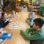 Bibliotekarka pokazuje grupie dzieci (3 dziewczynki jeden chłopiec) jedną z kart z których uczą się angielskich słówek.
