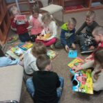 Dziesięcioro dzieci siedzi z książkami na podłodze i je przegląda.