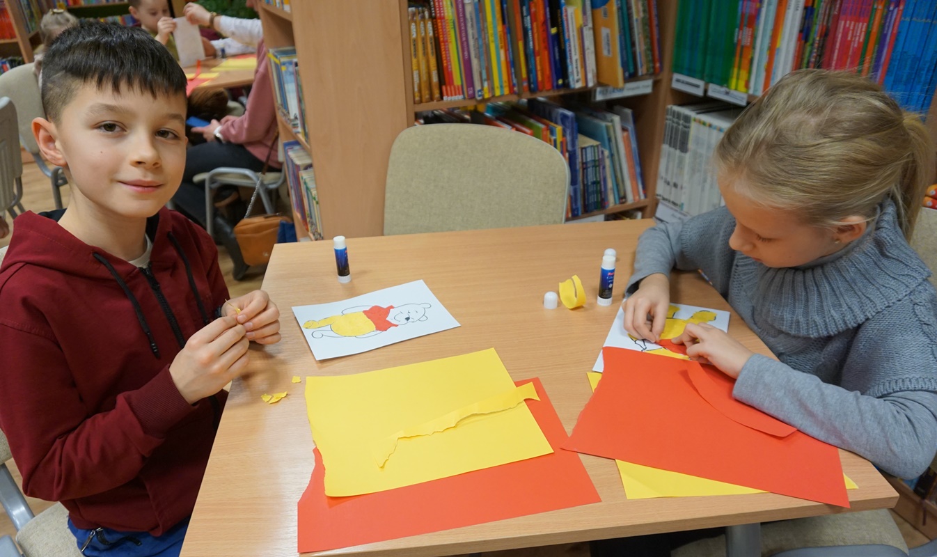dwoje dzieci wycina elementy z żółtych i czerwonych kartek papieru